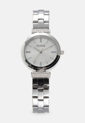 Sudraba nerūsējošā tērauda pulkstenis ar baltu ciparnīcu, kristāla akcentiem, apaļu korpusu un saistītu rokassprādzi. Iezīmē minimālistisku dizainu un skaidrus stundu rādītājus.