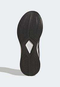 Suela de zapatilla deportiva negra con goma texturizada, cuenta con una sección blanca en forma de diamante y ranuras para tracción y estabilidad.