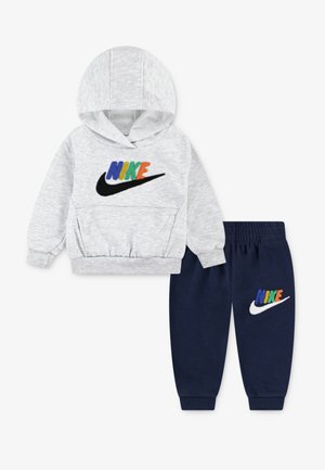 Sweatshirt à capuche gris avec un logo "NIKE" coloré ; associé à un jogging bleu marine avec un logo assorti. Tissu doux, poignets élastiques.