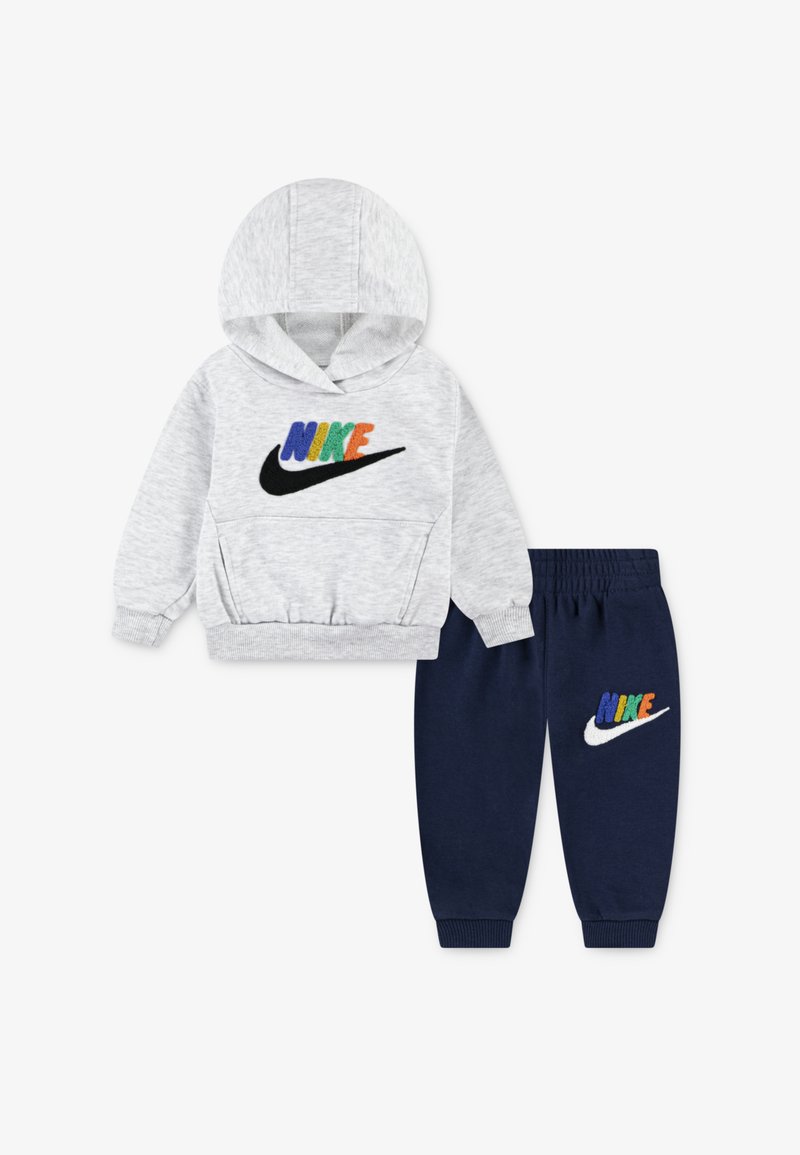 Huppari harmaalla huppukankaalla, jossa on värikäs "NIKE"-logo; yhdistettynä tummansinihin sweatpants-housuihin, joissa on vastaava logo. Pehmeä kangas, joustavat hihansuut.