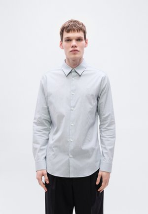 Koszula na guziki w jasnoniebieskim kolorze z pionowymi białymi paskami, posiadająca szpiczasty kołnierzyk, długie rękawy i luźny krój.