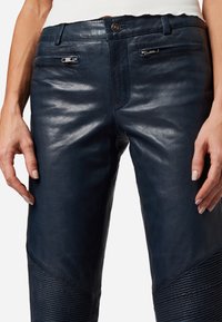Navy leren broeken hebben een gladde textuur met een aansluitend ontwerp, benadrukt door ribbeldetails bij de enkels en slanke zijzakken.