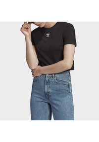 Svart bomullströja med korta ärmar och rundad halsringning, har en vit Adidas-logotyp på bröstet. Matchas med ljusblå denim jeans.