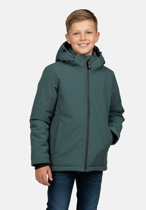 Jongen draagt een groene winterjas met capuchon en ritssluiting, handen langs het lichaam, glimlachend, tegen een effen lichtgrijze achtergrond.