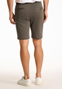 Grijze shorts met een gladde textuur, voorzien van twee achterzakken met knopen, omgezoomde mouwen en een getailleerd ontwerp. Draagt met witte sneakers.