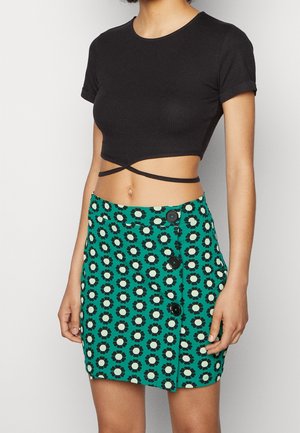 Haut court noir côtelé à manches courtes associé à une mini-jupe verte à motifs floraux avec des boutons noirs en accent.