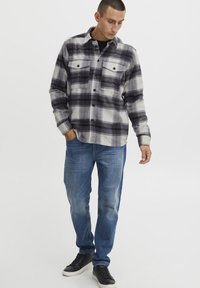 Geruite flanellen overhemd in grijs en zwart met twee borstzakken, knoopsluiting, gecombineerd met lichtblauwe spijkerbroek en zwarte sneakers.