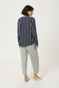 Camisa de rayas azul marino de manga larga con un corte relajado, combinada con pantalones tapered gris claro y zapatos de tacón de color claro.