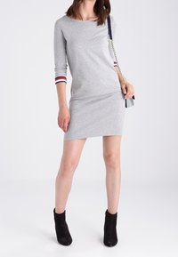 Abito grigio in jersey con maniche lunghe, polsini a strisce rosse e blu, slim fit, lunghezza al ginocchio, abbinato a stivali neri sopra la caviglia.