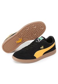 Mustad nubukist sneakers, millel kollane PUMA triip, kummist beež välispind koos mustriga tallaga ning mustad paelad kindla istuvuse tagamiseks.