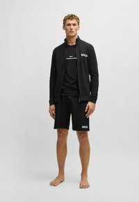 Completo sportivo nero composto da una giacca con zip, una t-shirt e pantaloni corti, tutti con il logo "BOSS" in bianco. Tessuto leggero.