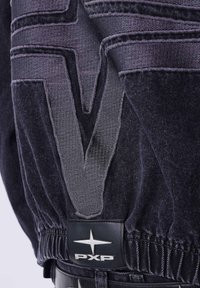 Donkere denim kledingstuk met een gestructureerd "V"-ontwerp en elastische tailleband. Voorzien van een zwart label met zilveren "PXP"-logo en steraccent.