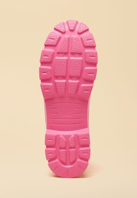 Pink gummisål med dybe mønstre og teksturerede greb designet til trækkraft på en beige baggrund.