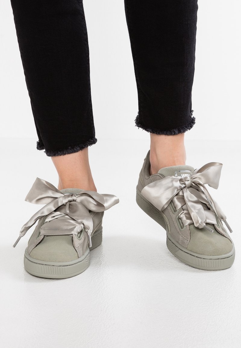 Las zapatillas verde claro cuentan con grandes cintas de seda gris para los cordones, un tejido suave y texturizado, y una suela de goma, combinadas con pantalones negros de dobladillo deshilachado.