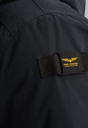 Crna jakna s teksturiranim materijalom, koja ima karakterističnu oznaku "PME LEGEND" u crnoj i žutoj boji te detalje sa trakama.