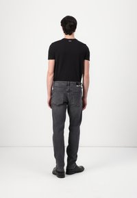 Tricou negru cu mânecă scurtă, având un logo pe spate, asociat cu blugi gri cu croială dreaptă, care au un patch pe spate și două buzunare laterale. Botine negre.
