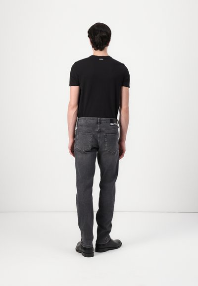 T-shirt noir à manches courtes avec logo au dos, associé à un jean droit gris avec un patch arrière et deux poches arrière. Bottes noires.