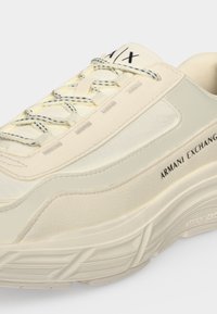 Ανδρικό sneaker Armani Exchange σε εκρού χρώμα με παχιά σόλα, υφασμάτινα πάνελ, κορδόνια με σχέδια και μαύρο λογότυπο στο πλάι και στη γλώσσα.