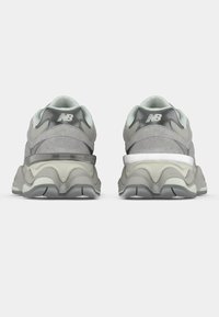 Γκρίζα αθλητικά παπούτσια με υφή στην επάνω πλευρά, διαθέτοντας μαξιλαρωμένο κολάρο, παχιά ενδιάμεση σόλα και αντίθετες μα�ύρες και λευκές λεπτομέρειες.