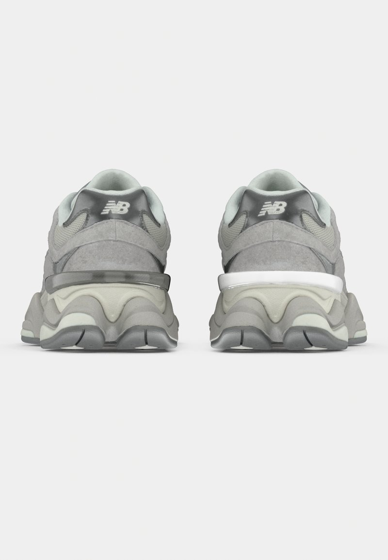 Graue Sportschuhe mit strukturiertem Obermaterial, die einen gepolsterten Schaft, eine dicke Zwischensohle und kontrastierende schwarz-weiße Akzente aufweisen.