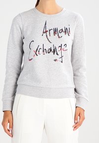 Felpa grigia con scollo rotondo e maniche lunghe, caratterizzata dal testo "Armani Exchange" in un design grafico multicolore. Materiale misto cotone.