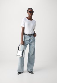 White short-sleeve tee, light blue wide-leg jeans, black belt, silver metallic handbag, and pointy black shoes, paired with oversized dark sunglasses.