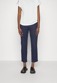 Pantalon bleu marine en mélange de coton, coupe droite avec une longueur légèrement raccourcie. Associé à un haut blanc à manches courtes et des sandales noires à enfiler.