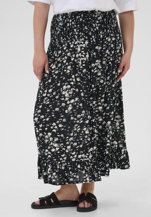 Black floral maxi skirt with a smocked waistband, white leaf patterns, and a ruffled hem. Paired with black slide sandals.