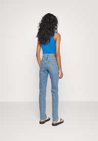 Top sin mangas azul combinado con unos vaqueros de mezclilla azul claro de tiro alto y sandalias negras, mostrando una silueta ajustada y un diseño clásico.