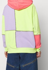 Color-blocked hoodie featuring pink, green, lavender, and yellow panels with contrasting stitching. Soft fabric with a relaxed fit.
