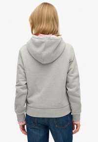 Grijze hoodie met een gevoerde capuchon, geribbelde boorden en zoom. Draagt over een roze shirt met lange mouwen, gecombineerd met blauwe spijkerbroek. Gladde katoenen textuur.