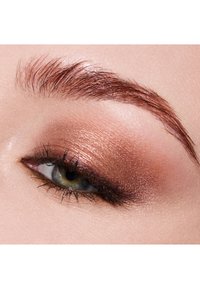 Zbliżenie na oko z ciepłym, metalicznym cieniem do powiek w kolorze miedzi, wyraźnymi rzęsami i wysmukloną brwią. Charakteryzuje się miękką, gładką teksturą skóry.