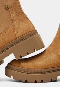 Botas de tobillo de ante marrón con una suela de goma gruesa y estriada y un upper texturizado. Presenta un detalle de botón en el lateral.