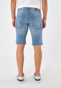 Lys blå denimshorts med rett snitt, med to baklommer og et lærmerke i midjen. Stoffet har en litt slitt tekstur.