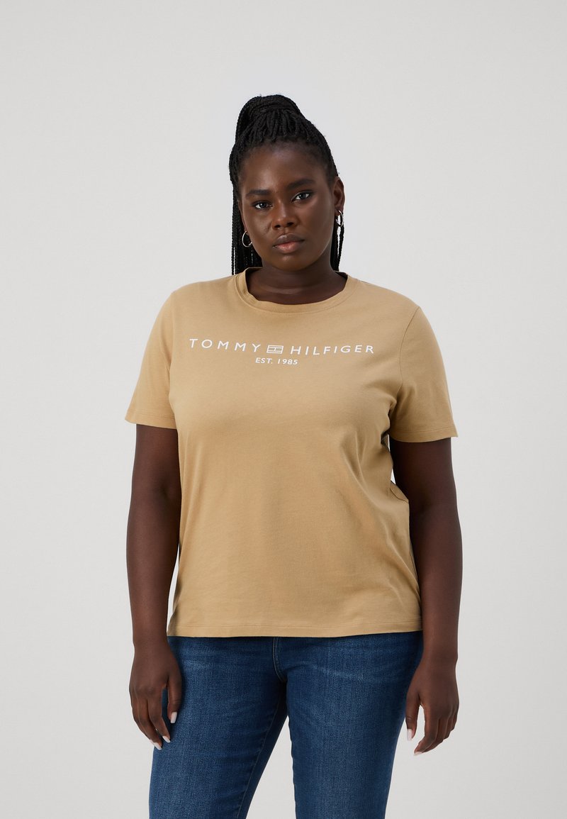 Béžové bavlnené tričko s krátkymi rukávmi a okrúhlym výstrihom, s bielym logom "TOMMY HILFIGER" a "EST. 1985." Pohľad z prednej strany.