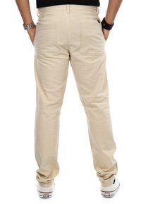 Beige Baumwollhosen mit geradem Bein, ausgestattet mit zwei Gesäßtaschen und einem sichtbaren Bund. Getragen mit weißen Turnschuhen.