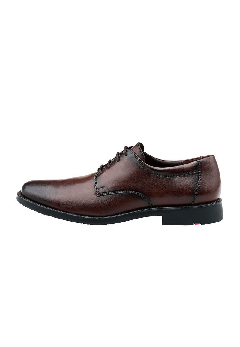 Zapato de vestir de cuero marrón con una textura suave, punta redondeada y cuatro ojetes para los cordones. Presenta una suela de goma negra y detalles de costura sutiles.