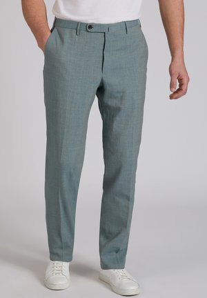 Uomo che indossa pantaloni azzurri sartoriali con chiusura a cerniera e bottone, abbinati a sneakers bianche casual e una camicia bianca.
