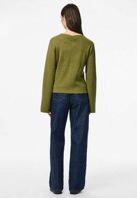 Zaļa adīta džemperis ar garām piedurknēm, apvienots ar tumši zilām platām biksēm. Džemperim ir apaļa kakla izgriezums un teksturēta auduma virsma.