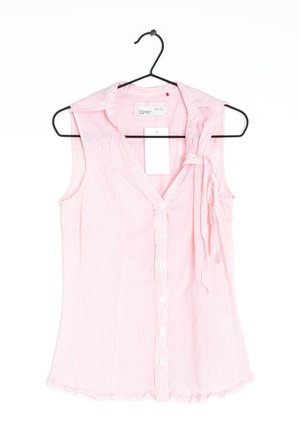 Blouse sans manches rose et blanche à fines rayures, avec des boutons sur le devant et un nœud noué sur l'épaule gauche, accrochée à un cintre noir.