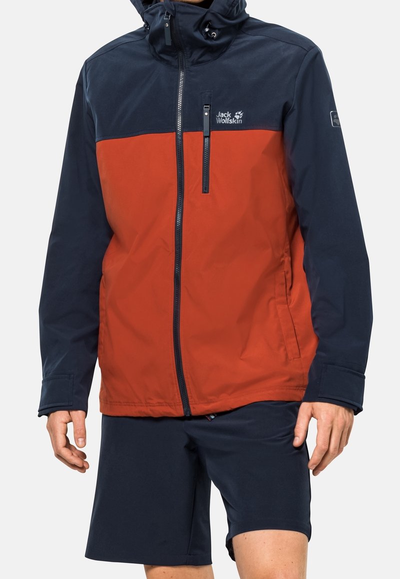 Röd och marinblå vattentät jacka med en central dragkedja, justerbar huva och logotyp på bröstet; tillsammans med marinblå shorts.