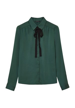 Blouse en soie verte avec un col classique, des manches longues et un nœud en ruban noir au cou. Comprend une fermeture à boutons à l'avant et des détails plissés.