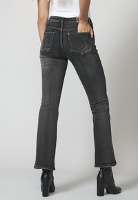 Jeans de mezclilla negra acampanados con cintura de altura media, que incluyen dos bolsillos traseros con costuras decorativas y detalles de dobladillo sin terminar en la pierna.