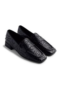 Mocassins en cuir noir avec un design clouté, présentant un bout carré et un talon bas. Texture lisse avec une sangle décorative sur le dessus.