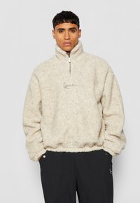 Kremfarget fleece-pullover med høy krage, halv-lås og brodert logo. Myk tekstur, avslappet passform og elastiske mansjetter.