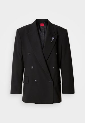 Kaksirivinen musta bleiseri suurilla napeilla, lovettuna käänteillä ja teksturoidulla vuorilla. Sisältää koristeellisen rintaneulan käänteessä.