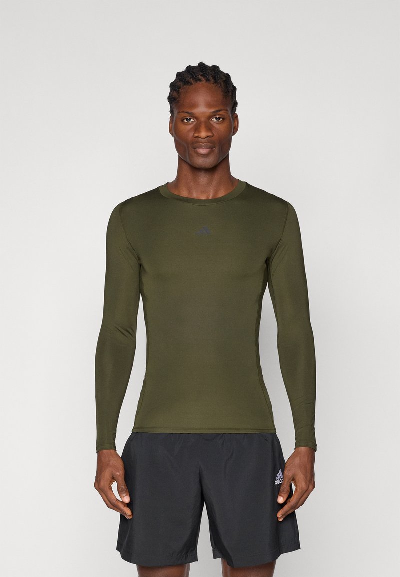 Dlouhý rukáv, olivově zelený sportovní top se slim fit střihem, vyrobený z lehkého materiálu, s malým černým logem na hrudi.