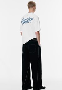 Hvid bomulds T-shirt med blåt ternet grafisk mønster på bagsiden. Kombinationen med sorte wide-leg bukser med kontraststing og lommer.