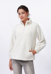 White fleece pullover with a half-zip collar, two buttons, and side pockets. Features a soft texture and relaxed fit.