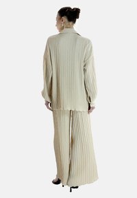 Ensemble en deux pièces de couleur beige clair, texturé, comprenant une chemise à manches longues et un pantalon à jambe large avec un motif en losange. Ourlet surpiqué et coupe ample.